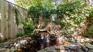 Ein kleiner Wasserfall in einem Garten mit einem Holzzaun und Steinstufen, die hinaufführen.