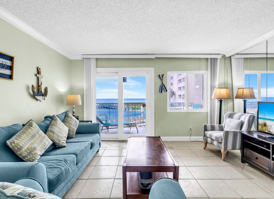 A living room with a sofa, armchairs, a coffee table, and a TV. There is a balcony with a view.