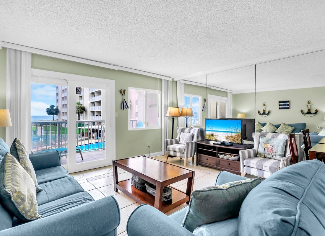 Un salon comprenant un ensemble de canapés, un téléviseur, une table basse et une vue sur une piscine et des immeubles, visible à travers les portes vitrées.