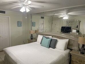 A hotel room with a large bed, two bedside tables, a ceiling fan, a large mirror, and a door.