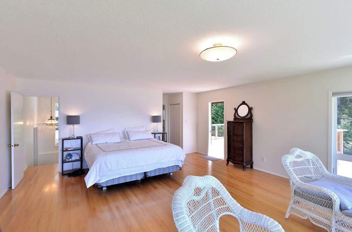 A spacious bedroom with a large bed, two bedside tables, a wardrobe, and wicker chairs.