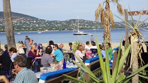 Een restaurant aan de kust met terras, met uitzicht op zee en een zeilboot.