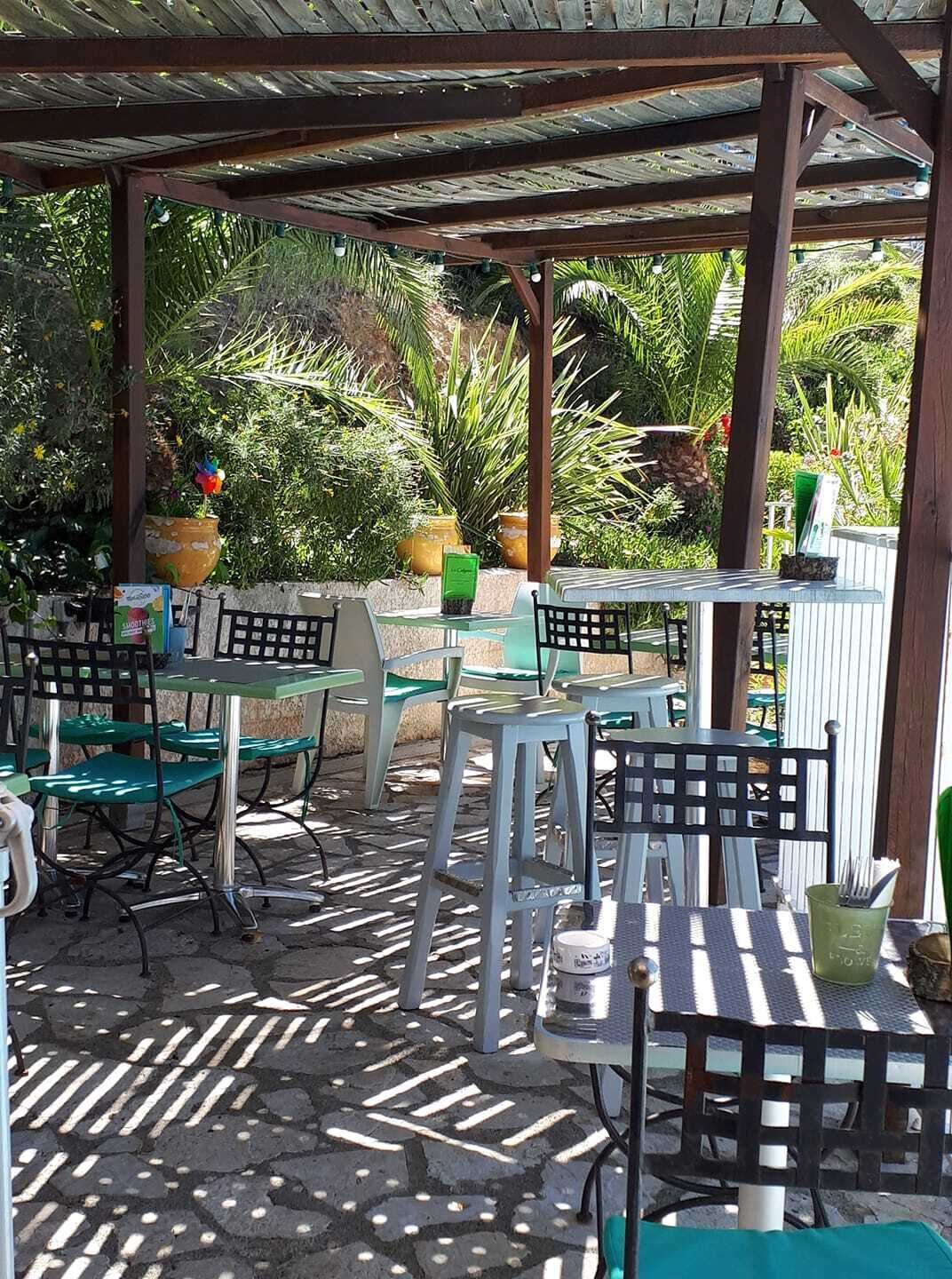 Een terras buiten met tafels en stoelen, omringd door groen en een houten pergola.