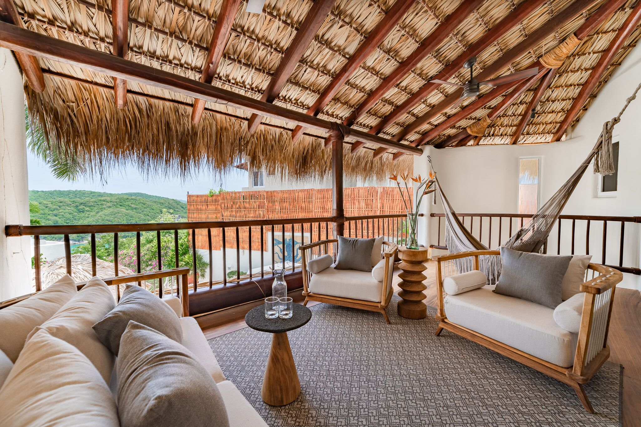 Una habitación con techo de paja, una hamaca, un sofá y vistas al verdor.