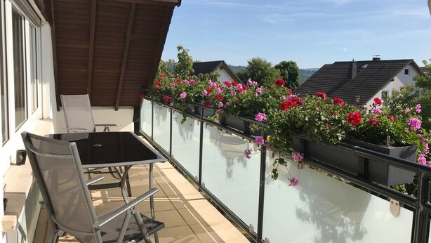 Een balkon met glazen hekwerk, een tafel en twee stoelen.