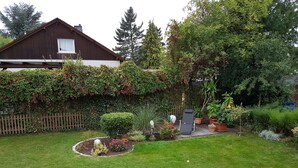 Een goed onderhouden tuin met gazon, houten omheining en diverse planten en bomen.