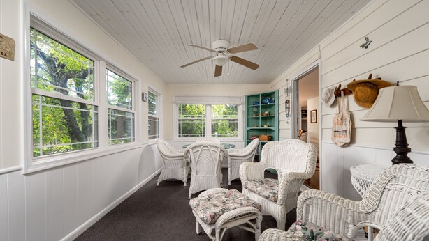 A room with white paneled walls, a ceiling fan, wicker furniture, and large windows offering a view of trees. - Large home in Broadkill.  Just a block to the beach! 907 N Bayshore (Milton)