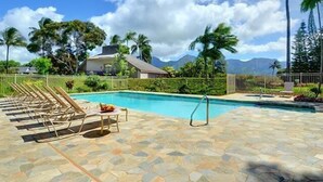 Un espace piscine doté de chaises longues, d’une terrasse carrelée en pierre et offrant une vue sur les montagnes et les palmiers.