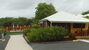 A building with a covered patio area, a paved walkway, and a garden with shrubs and flowers.