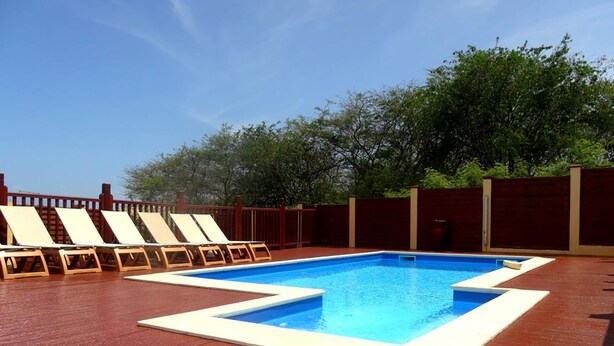 A rectangular swimming pool with a wooden deck surrounding it, equipped with lounge chairs.