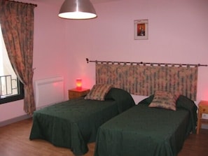 Une chambre avec deux lits simples, une table de chevet avec une lampe, une fenêtre avec des rideaux et une affiche accrochée au mur.