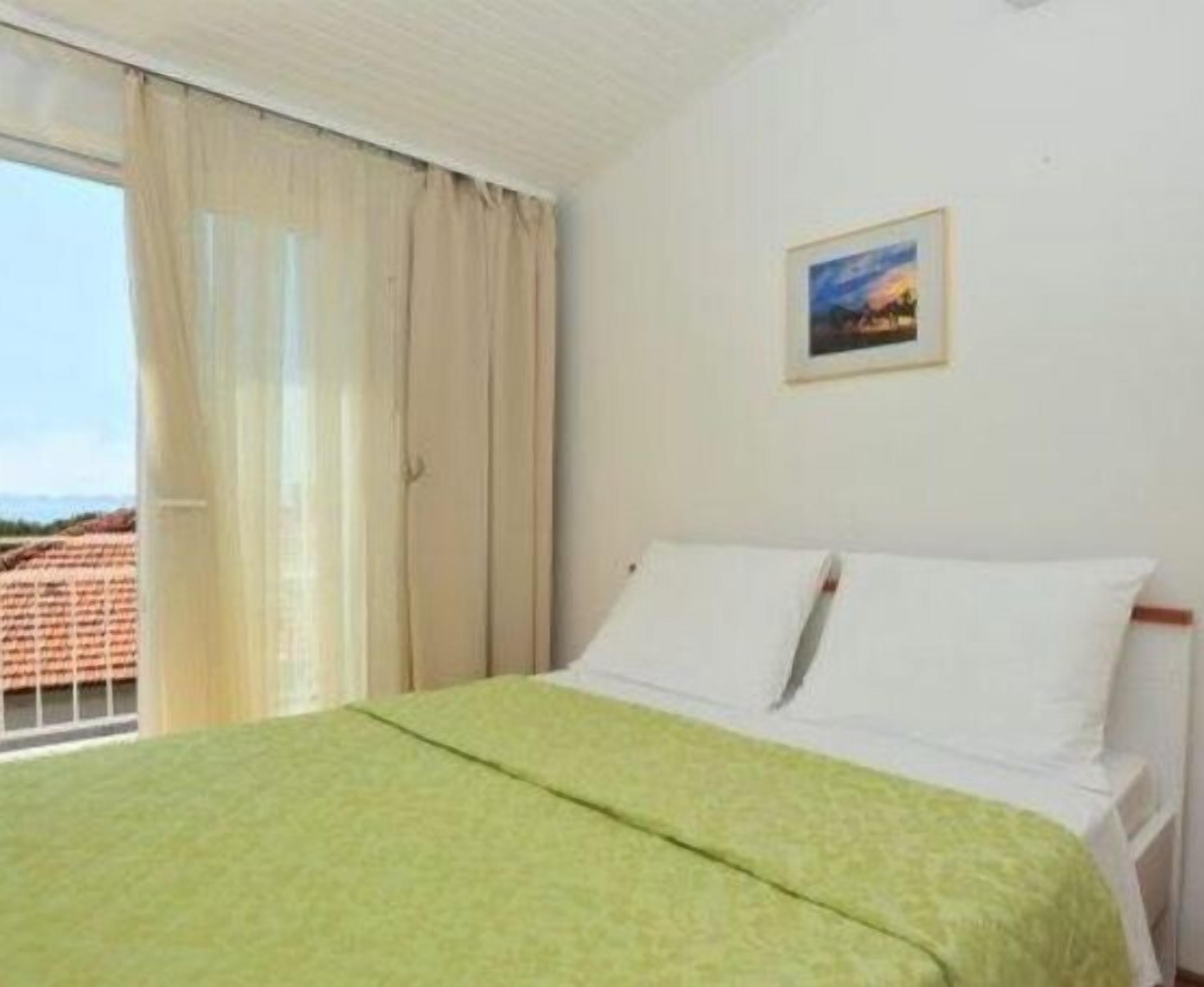 A hotel room with a bed, a window with curtains, and a painting on the wall.