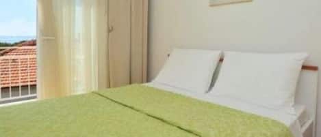 A hotel room with a bed, a window with curtains, and a painting on the wall.