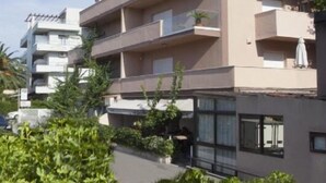 Un edificio de varios pisos con balcones, una entrada cubierta y abundante vegetación alrededor.