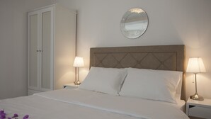 Una cama bien hecha con sábanas blancas y dos almohadas, flanqueada por mesitas de noche con lámparas, un armario y un espejo en la pared.
