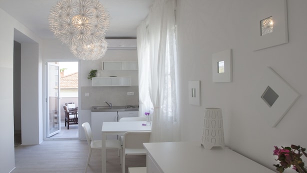 Una cocina moderna y minimalista con armarios blancos, un comedor con sillas blancas y una lámpara colgante.