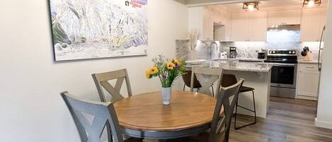 Un comedor con una mesa redonda de madera y sillas, un jarrón con flores y una pintura de Jackson Hole en la pared.