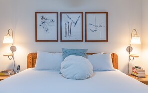 Quarto de hotel com uma cama, duas luminárias fixadas na parede e três quadros enquadrados.
