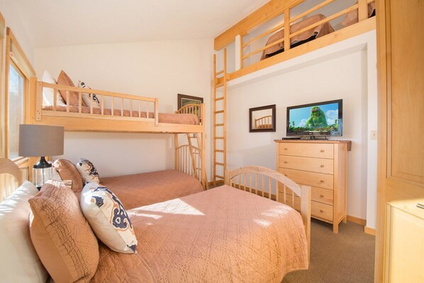 A bunk bed room with a television, a desk, and a chair.