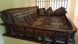 Un canapé doté d’un motif matelassé et de pieds en bois, placé contre un mur, avec une fenêtre en arrière-plan.