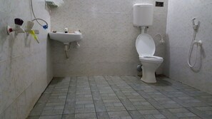 Une petite salle de bain carrelée, équipée de toilettes, d’un lavabo et d’une douche.
