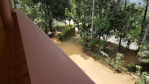 Une vue depuis un balcon donnant sur un chemin de terre bordé d’une végétation luxuriante et d’arbres.
