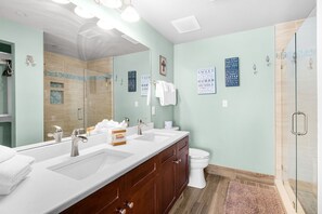 A bathroom with a large mirror, two sinks, a toilet, and a shower area. - 0507 - Fresh and Fun Coastal Condo (Panama City Beach)