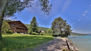 Ein Chalet mit Balkon, umgeben von üppiger Vegetation und einem Seeblick.