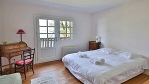 Ein Schlafzimmer mit Holzboden, einem Bett mit weißer Bettwäsche, einem Schreibtisch mit Stuhl, einem Fenster mit Aussicht und einer Heizung.