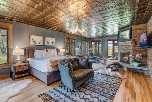 A bedroom with a large bed, a sofa, a fireplace, and a ceiling with a geometric pattern.