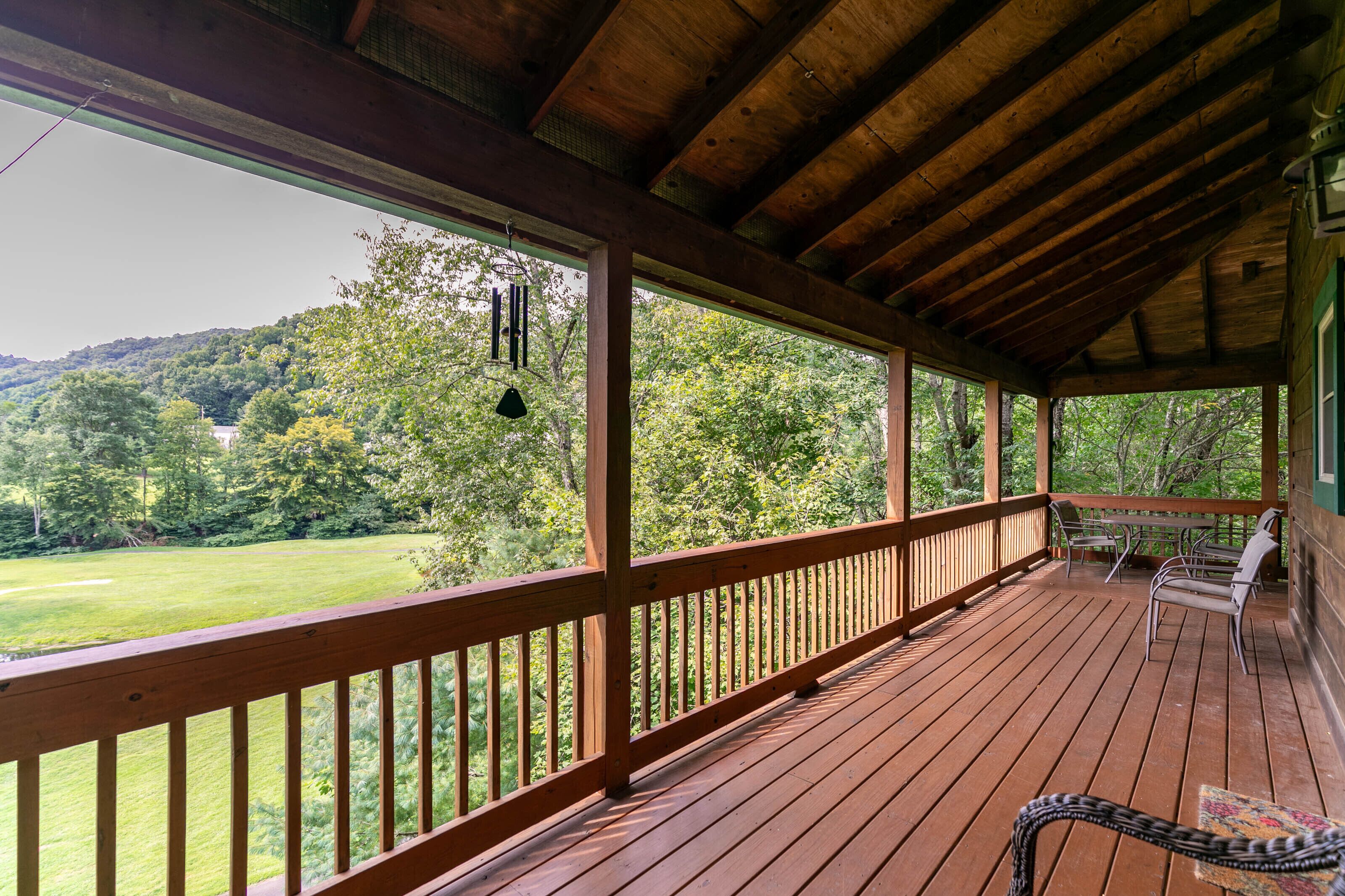 A wooden deck with a railing, a hanging light fixture, and a view of a green landscape.