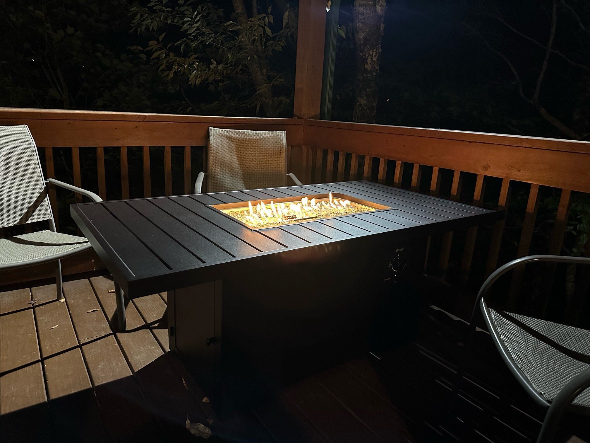 A deck with a rectangular table and chairs, a built-in fire feature, and a wooden railing.