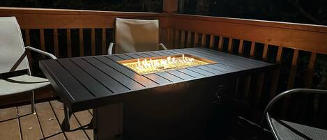 A deck with a rectangular table and chairs, a built-in fire feature, and a wooden railing.
