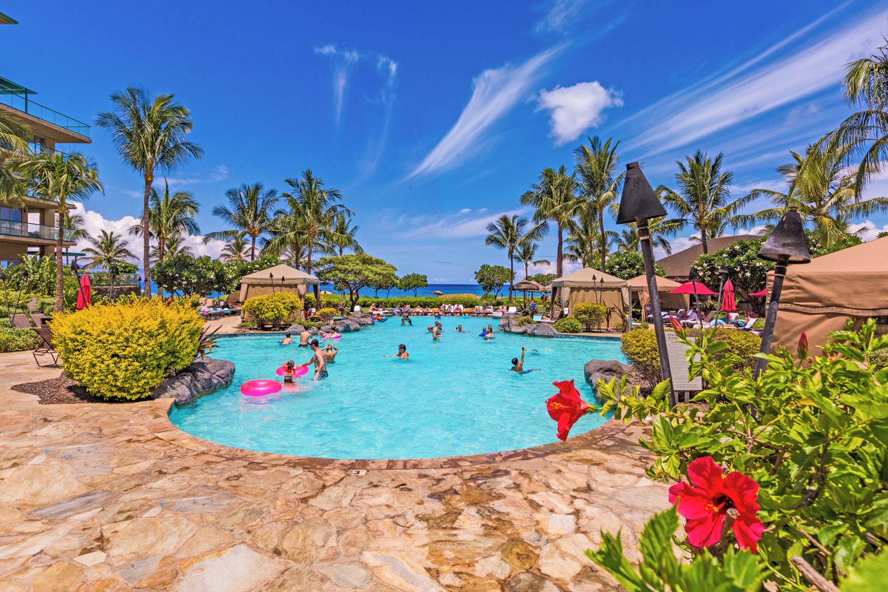 A pool area with clear blue water, surrounded by palm trees and lounge chairs.