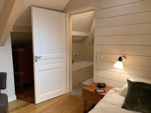 A bedroom with a bed, bedside table, lamp, and a door leading to a bathroom. - Lake Annecy Veyrier du lac Villa Marianne 8 people lakeside swimming pool (Veyrier du lac)