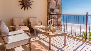 A balcony with a view of the beach, featuring a swan sculpture, two chairs, a table, and a decorative sun on the wall. - Sonoran Sky 502 Absolute Beach Paradise Haven Oceanfront Condo (Puerto Penasco)