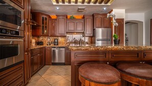A kitchen with wooden cabinets, stainless steel appliances, granite countertops, and a central island with stools. - Sonoran Sky 502 Absolute Beach Paradise Haven Oceanfront Condo (Puerto Penasco)