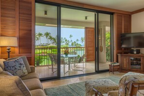 A modern living room with a sofa, a television, and a dining area with a table and chairs. - Mauna Lani Terrace E201 (Kamuela)