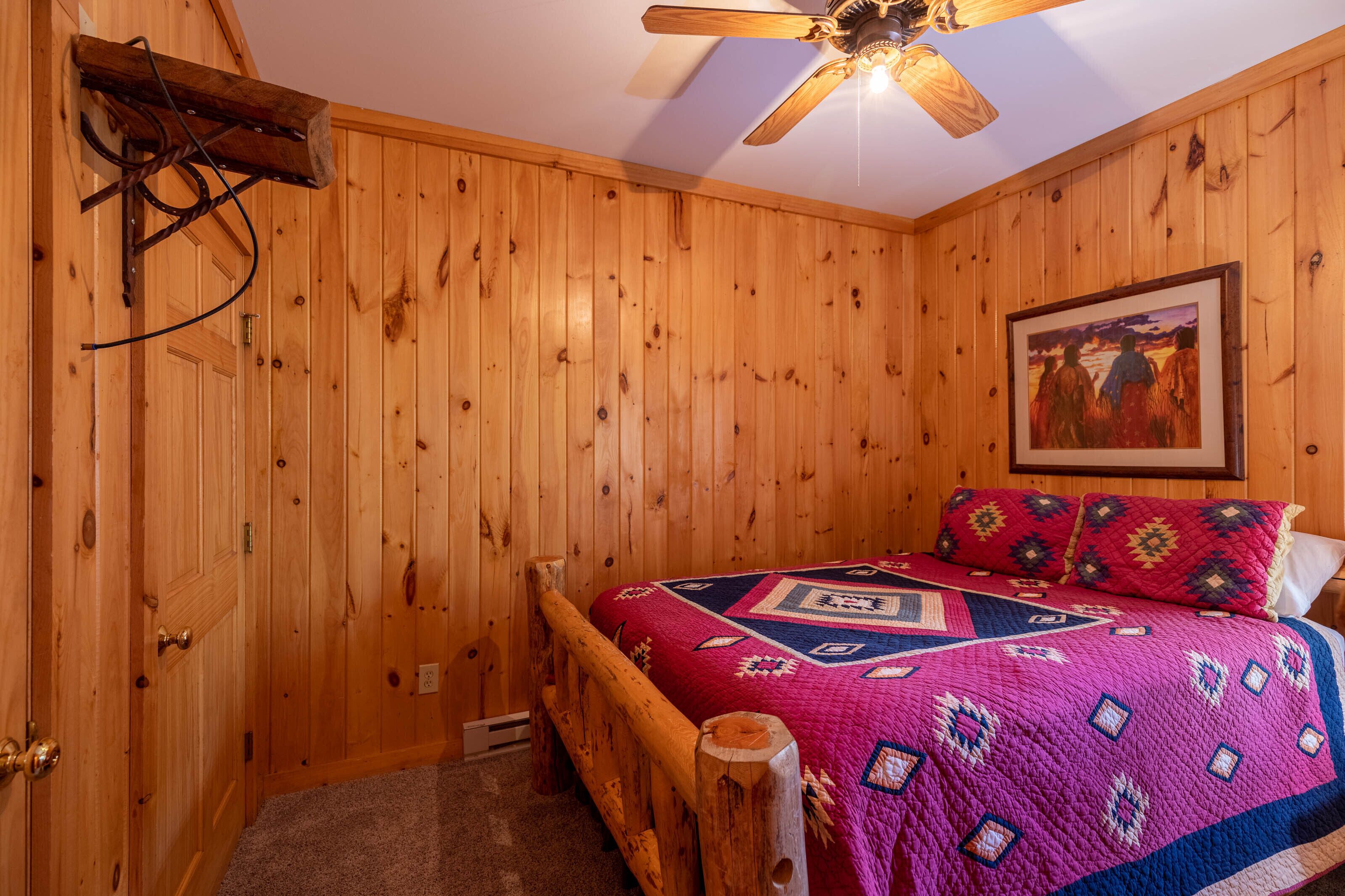 A wooden-paneled room with a bed, a ceiling fan, and a painting on the wall.