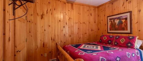 A wooden-paneled room with a bed, a ceiling fan, and a painting on the wall.