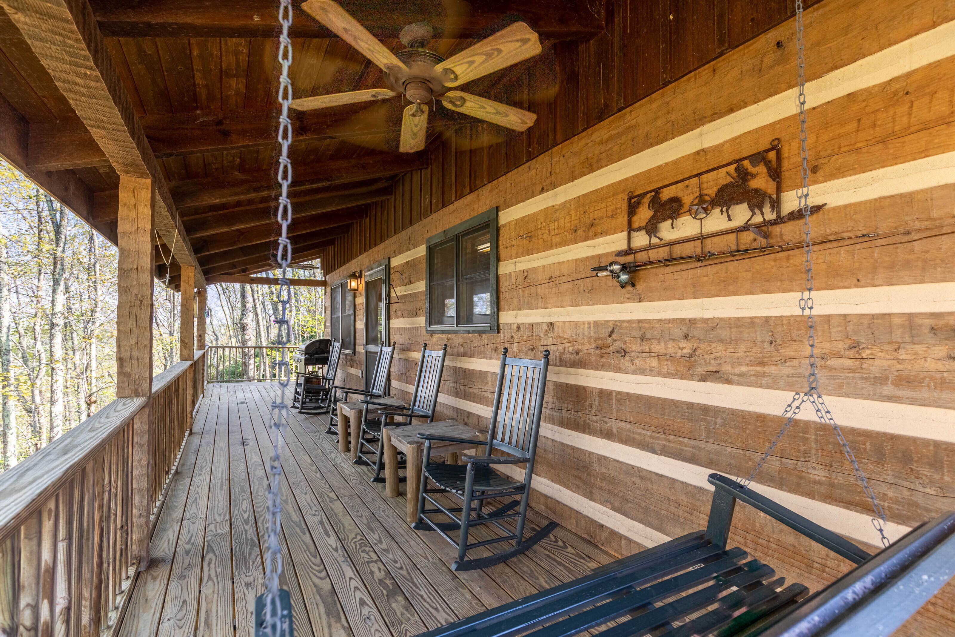 A wooden cabin with a porch, rocking chairs, and a ceiling fan.