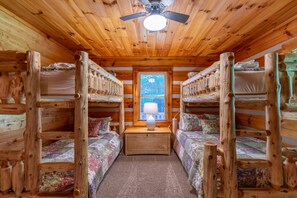 A cabin interior with wooden bunk beds, a central table with a lamp, and a ceiling fan. - Hemlock Hideaway: Quiet Neighborhood Cabin Near Boone & Blowing Rock with Firepit, Yard, & Hot Tub! (Boone)