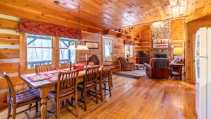 Een houten chalet interieur met een eethoek, open haard en een wand van natuursteen.