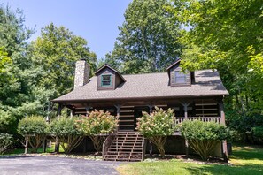A log cabin with a chimney, a porch, and a small staircase leading to the entrance. - Hemlock Hideaway: Quiet Neighborhood Cabin Near Boone & Blowing Rock with Firepit, Yard, & Hot Tub! (Boone)