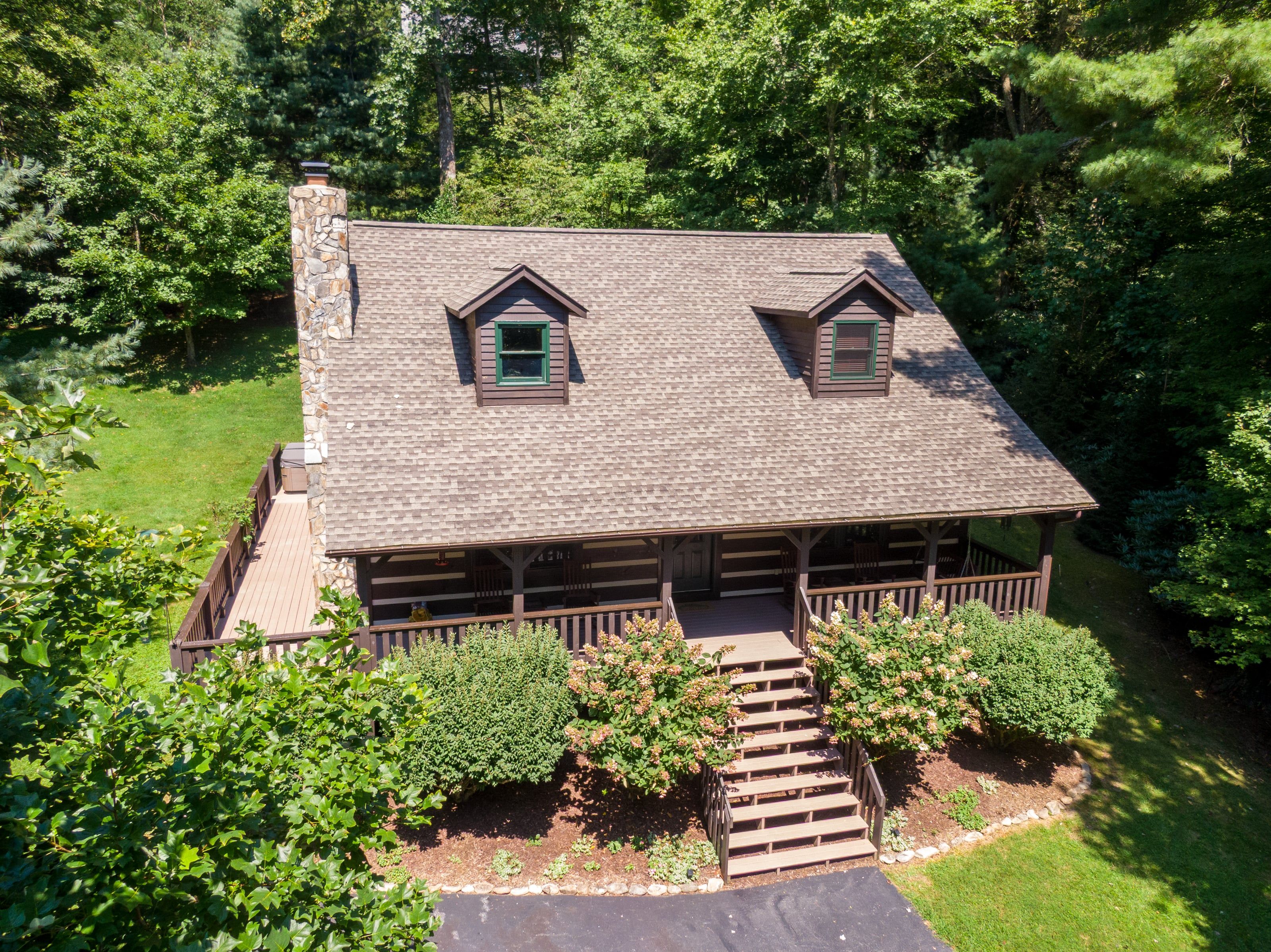 A two-story log cabin with a stone chimney, a covered porch, and a small front yard with a wooden staircase leading to the entrance.