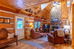 A cozy log cabin interior with a stone fireplace, wooden furniture, and a television. - Hemlock Hideaway: Quiet Neighborhood Cabin Near Boone & Blowing Rock with Firepit, Yard, & Hot Tub! (Boone)