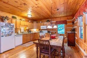 A wooden cabin interior with a dining table, chairs, a refrigerator, and a kitchen area. - Hemlock Hideaway: Quiet Neighborhood Cabin Near Boone & Blowing Rock with Firepit, Yard, & Hot Tub! (Boone)
