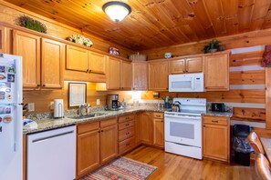 A kitchen with wooden cabinets, a microwave, a stove, and a coffee maker. - Hemlock Hideaway: Quiet Neighborhood Cabin Near Boone & Blowing Rock with Firepit, Yard, & Hot Tub! (Boone)