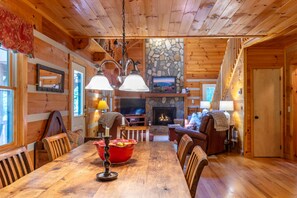 A wooden interior with a dining table, chairs, a fireplace, and a stone wall. - Hemlock Hideaway: Quiet Neighborhood Cabin Near Boone & Blowing Rock with Firepit, Yard, & Hot Tub! (Boone)