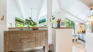 A modern kitchen with wooden cabinetry, a large window, and a dining area with white chairs. - Pali Uli 8, The Gem, honeymoon or romantic getaway (Princeville)